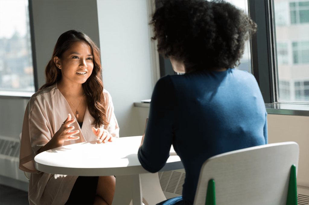 Performance review examples: two women sitting on a white table and talking 